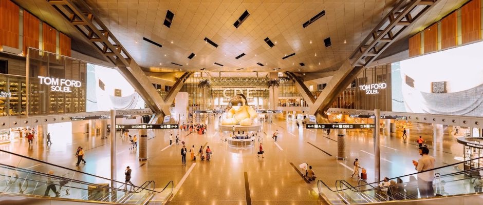 Spacious modern airport terminal with people walking and a large golden teddy bear sculpture at the center.
