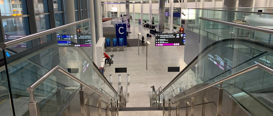 View down escalators inside a modern airport terminal with signage for international arrivals and gate C visible.