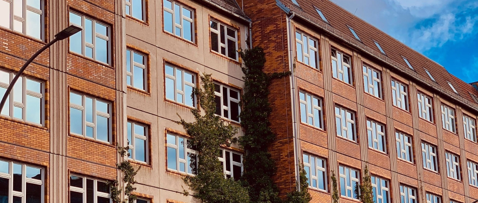 Multi-story brick and concrete commercial building with numerous windows and climbing ivy, under a blue sky with some clouds.
