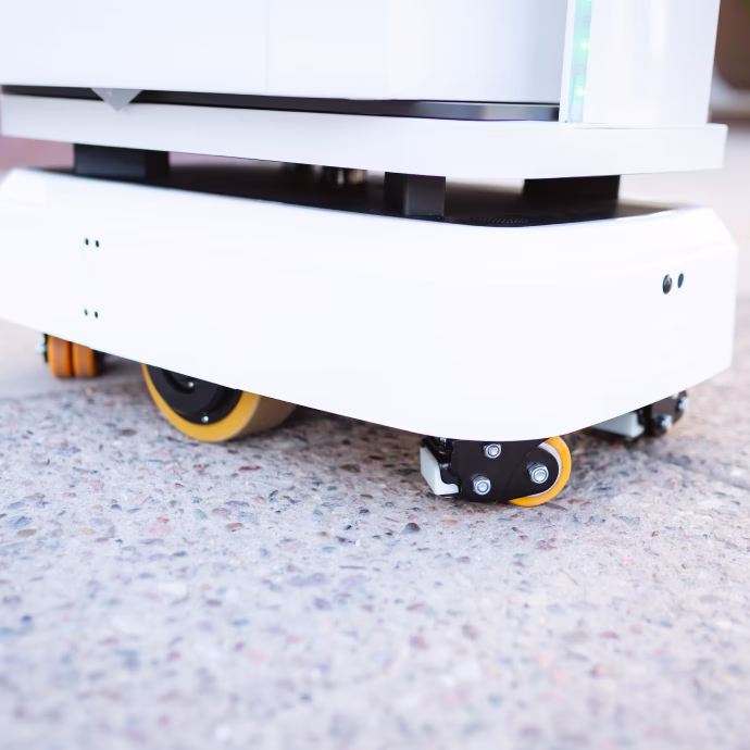 Close-up of a white commercial-grade automated mobile robot base with yellow caster wheels on a textured floor.