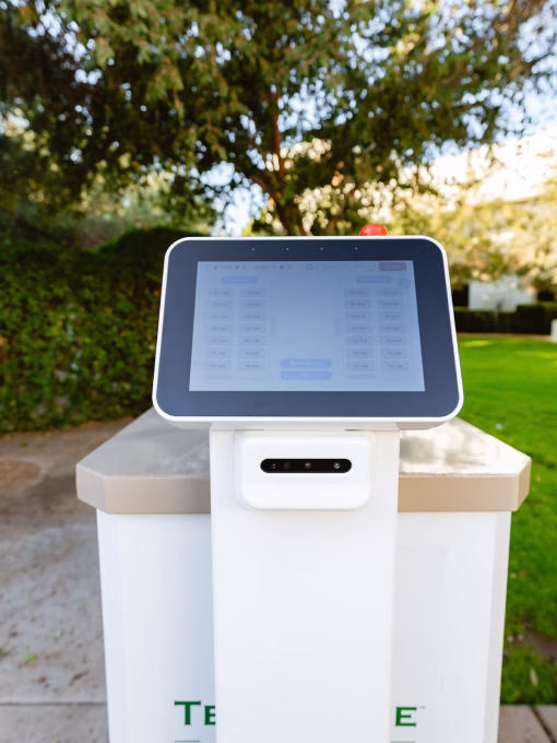 Close-up of a white robotic control panel with a touchscreen interface outdoors, with trees and grass in the background.