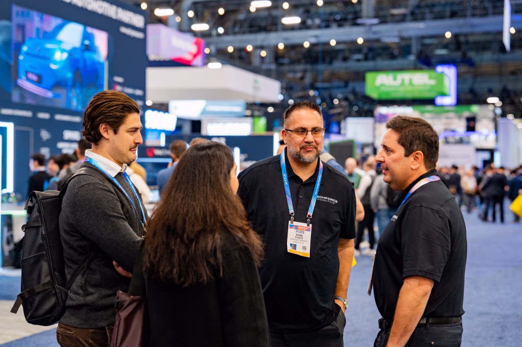 Four people wearing conference badges engaged in conversation at a technology trade show.