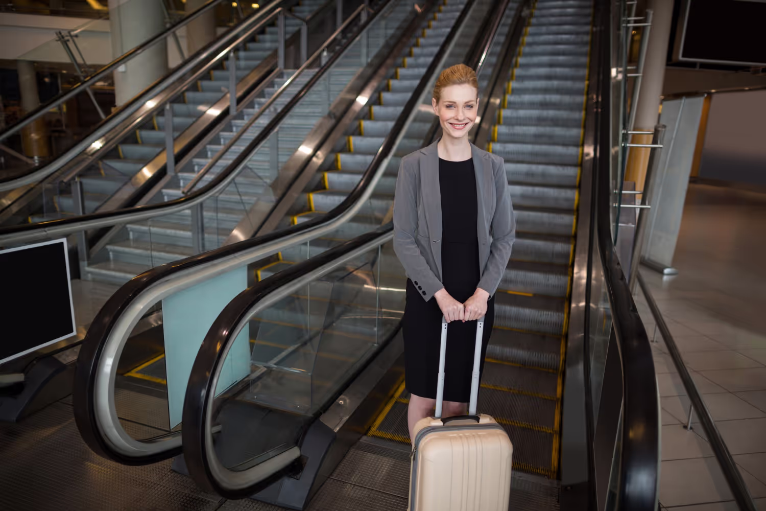 A woman is standing on a escalator with a suitcase.