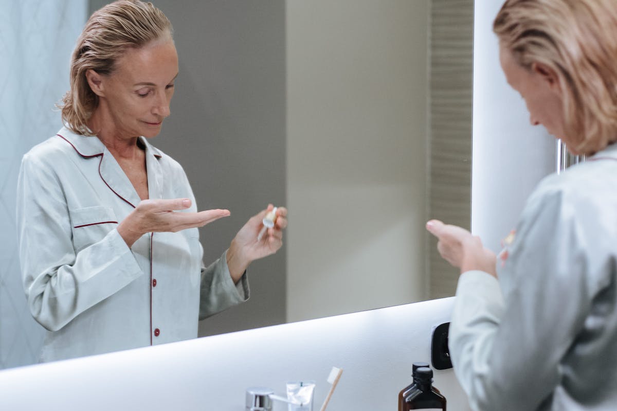 Senior woman applying skincare serum in front of bathroom mirror during her morning routine