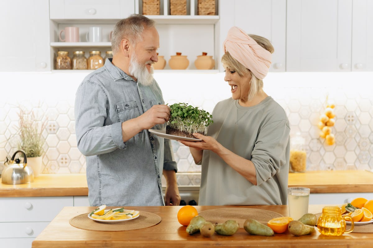 Happy senior couple smiling and holding a plate of fresh microgreens in a cozy kitchen setting