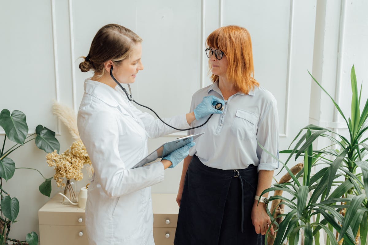 A doctor using a stethoscope to check the heart of a woman patient during a clinical visit