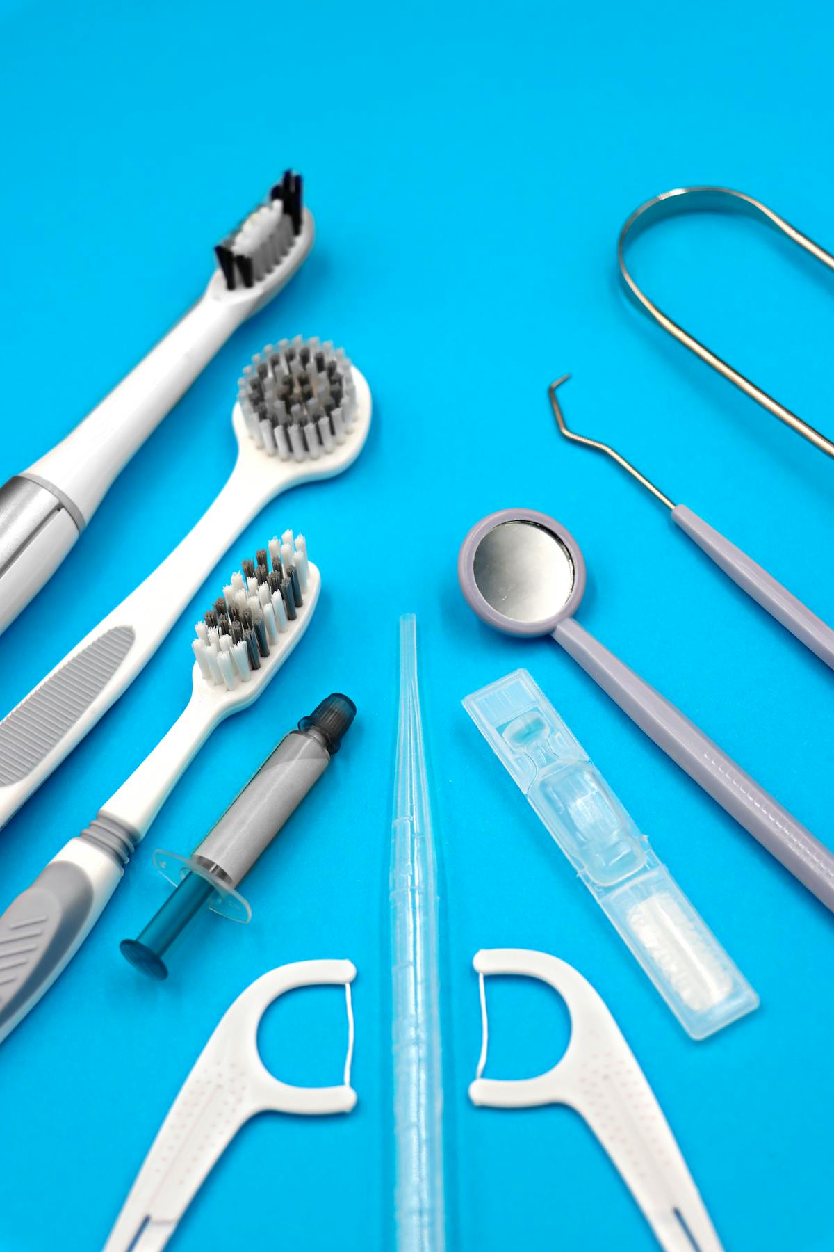 An assortment of dental hygiene tools including toothbrushes, floss, and dental picks arranged neatly on a flat blue background