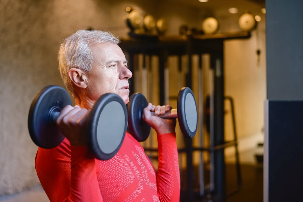An elderly man lifting dumbbells in a gym, demonstrating strength training for healthy aging