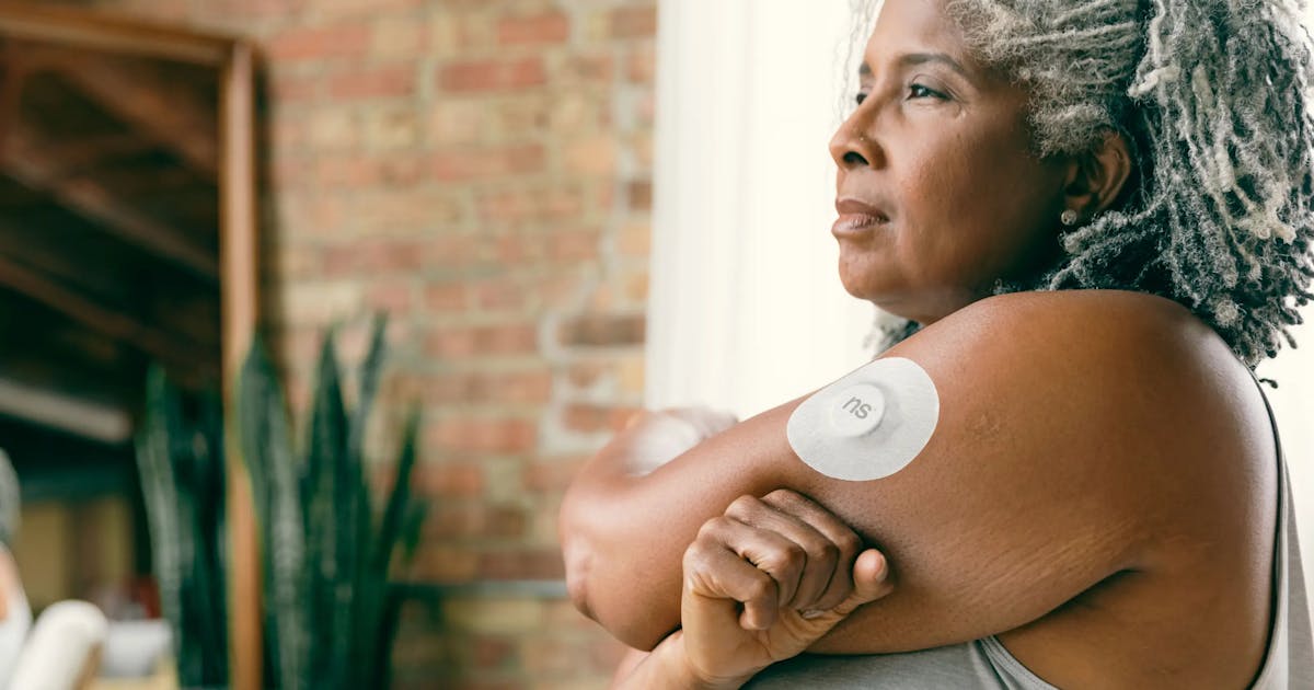 A mature woman with gray hair wearing a continuous glucose monitoring device on her arm