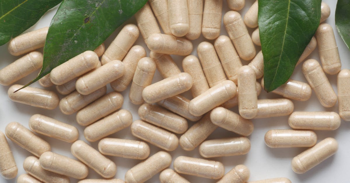 Organic medicine capsules with fresh green leaves on a white background