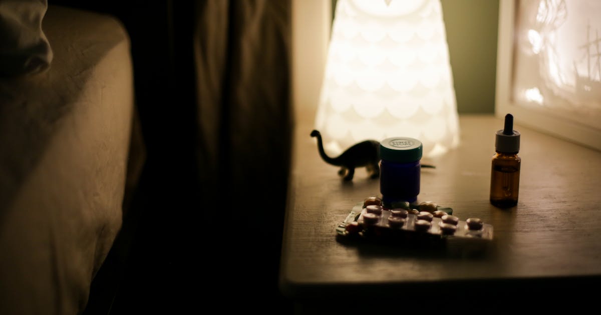 Medicine bottles and pill packets on a dimly lit bedside table in a calm bedroom