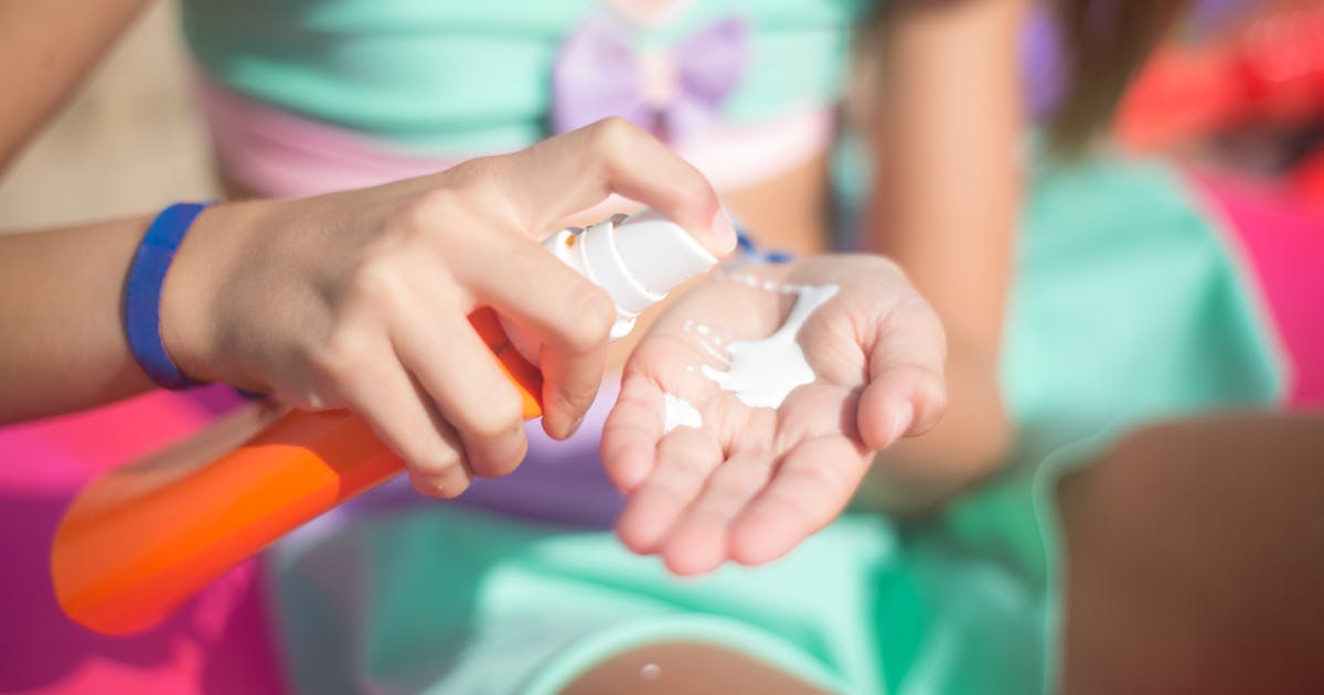 A woman spraying a sunscreen lotion on her palm outdoors in a natural setting