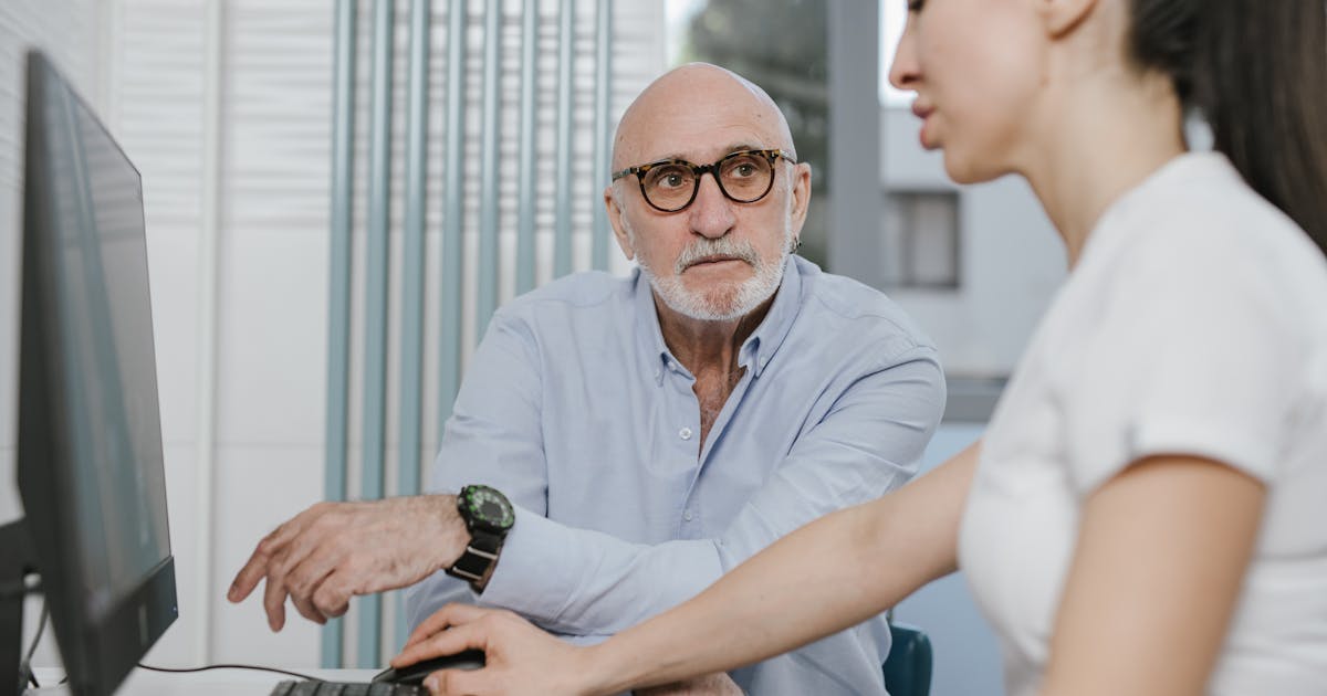 An elderly man wearing eyeglasses receiving a consultation from a medical practitioner