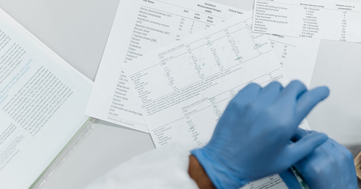 Gloved hands reviewing printed lab test results on a white surface