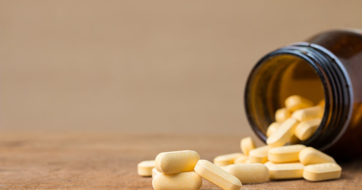 Yellow tablets spilling from an open brown glass bottle on a wooden surface