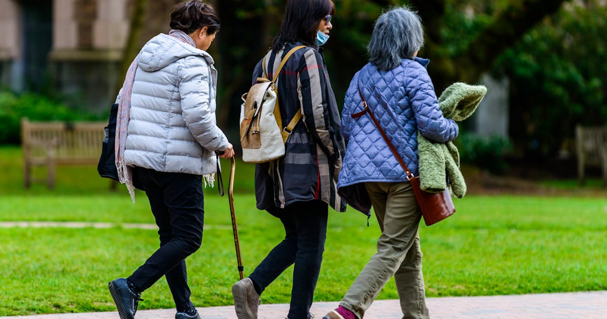 Three women walk together in a park dressed in warm jackets on a fall day
