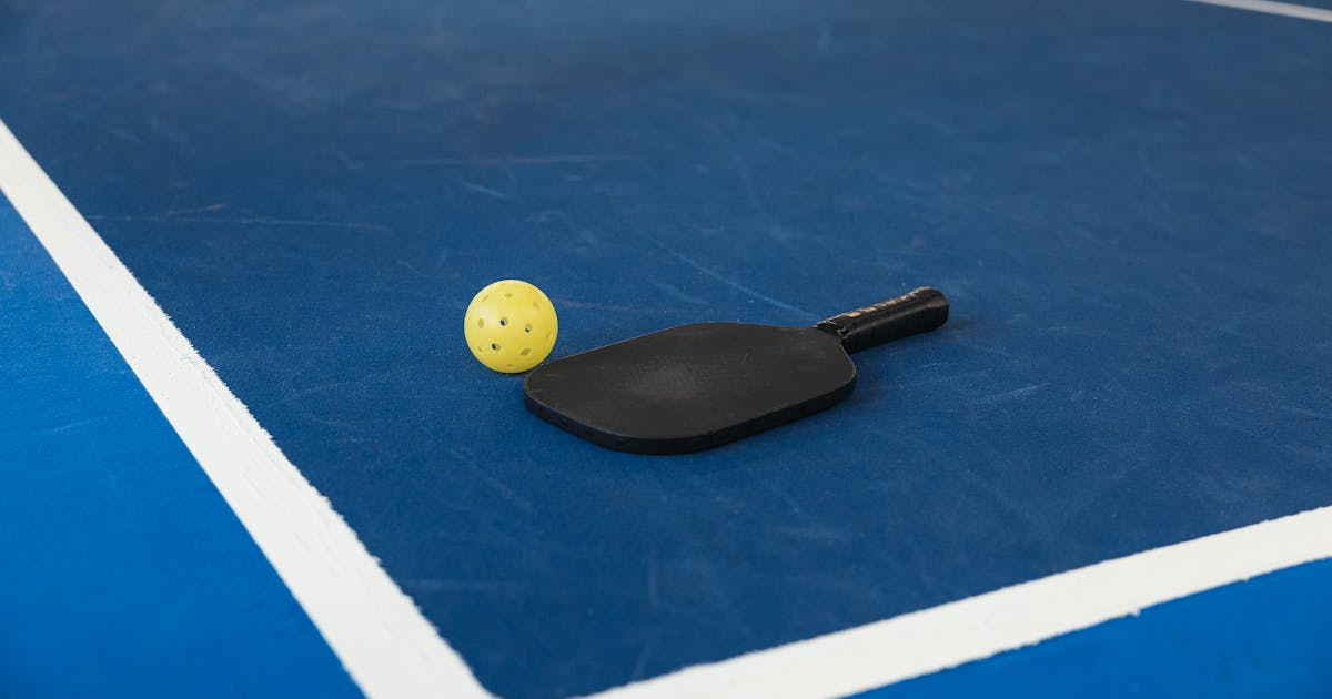 A pickleball paddle and yellow ball resting on a blue pickleball court with white lines