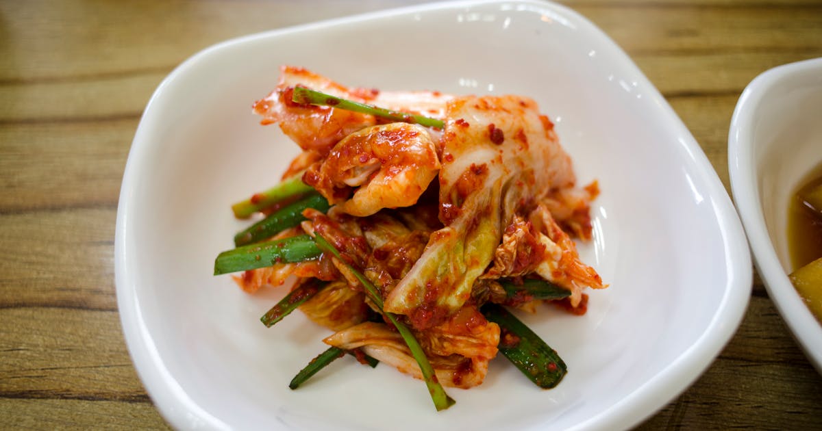 Close-up of traditional Korean kimchi served in a white ceramic dish on a wooden table