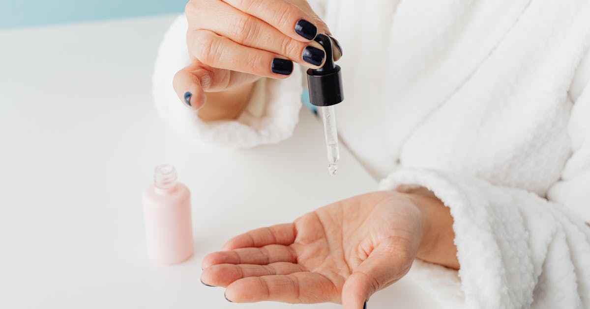 Close-up of a woman applying skincare serum from a dropper onto her hand in a studio setting