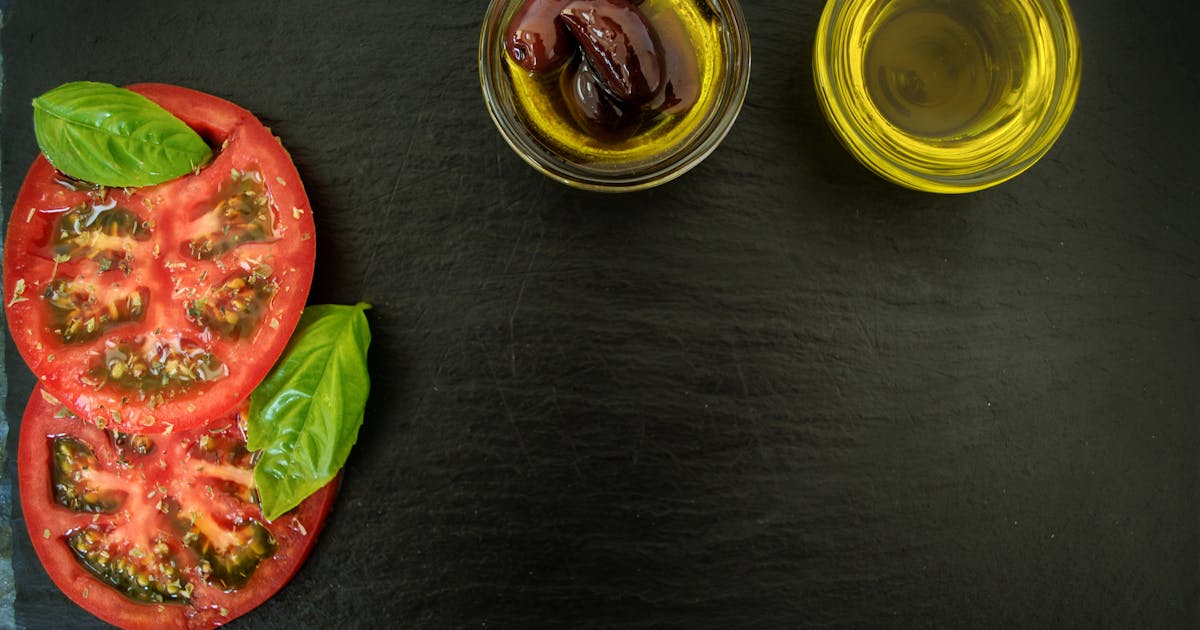 Top view of fresh basil, sliced tomatoes, olives, and olive oil on slate, perfect for Italian cuisine themes
