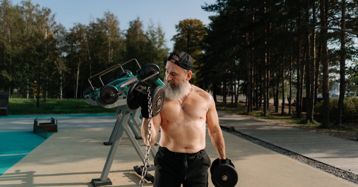 A senior man exercises outdoors with dumbbells, embracing a healthy fitness routine