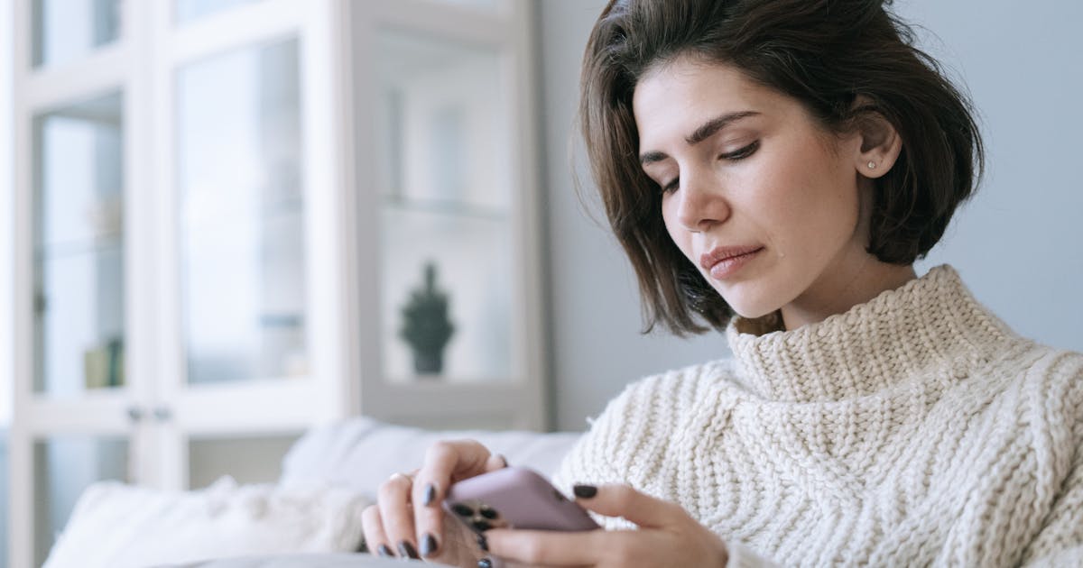 Woman in cozy knitted sweater using smartphone at home with a serene expression