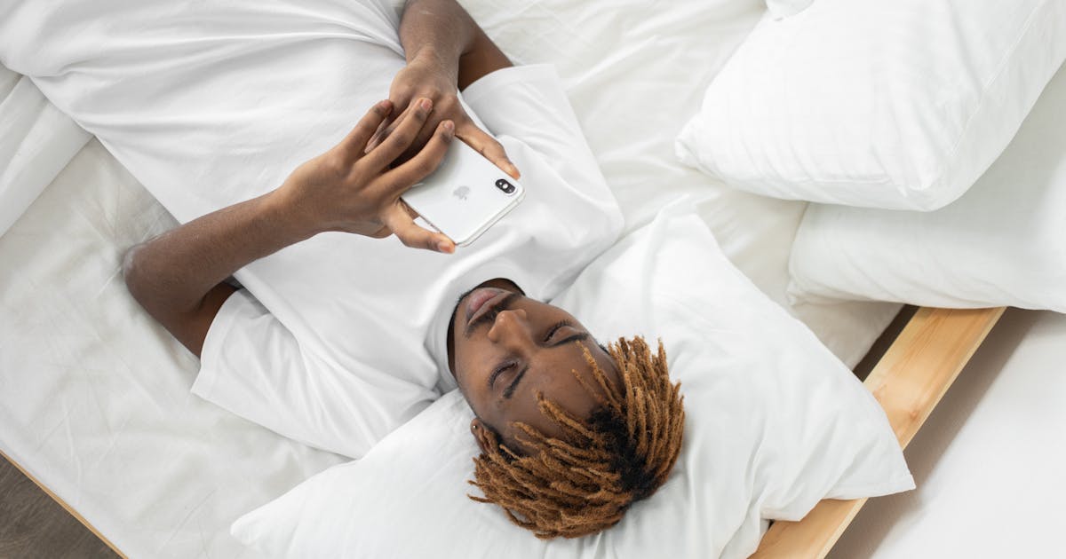 Young man lying in bed texting on smartphone, relaxed setting