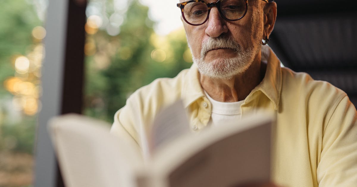 Elderly man with eyeglasses focused on reading a book outside