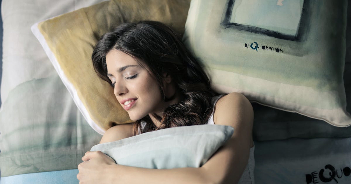 Woman peacefully sleeping in bed, hugging a pillow with a contented smile