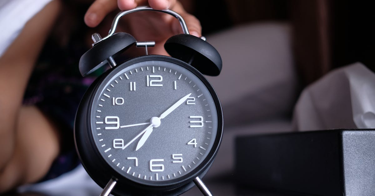 A hand reaches out to turn off an analogue alarm clock in the early morning