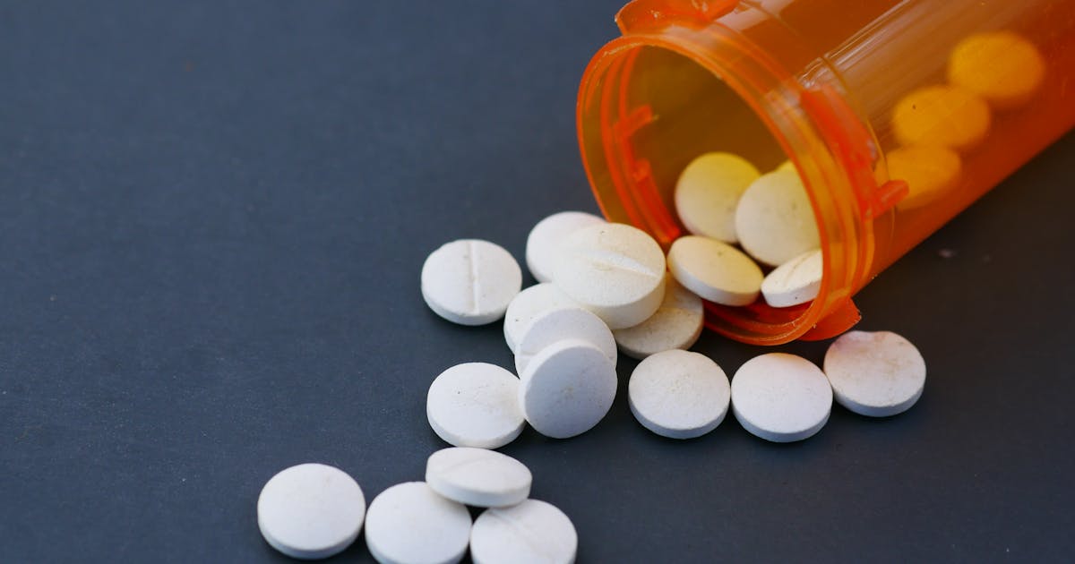 Close-up of white pills scattered from an orange prescription bottle on a gray surface