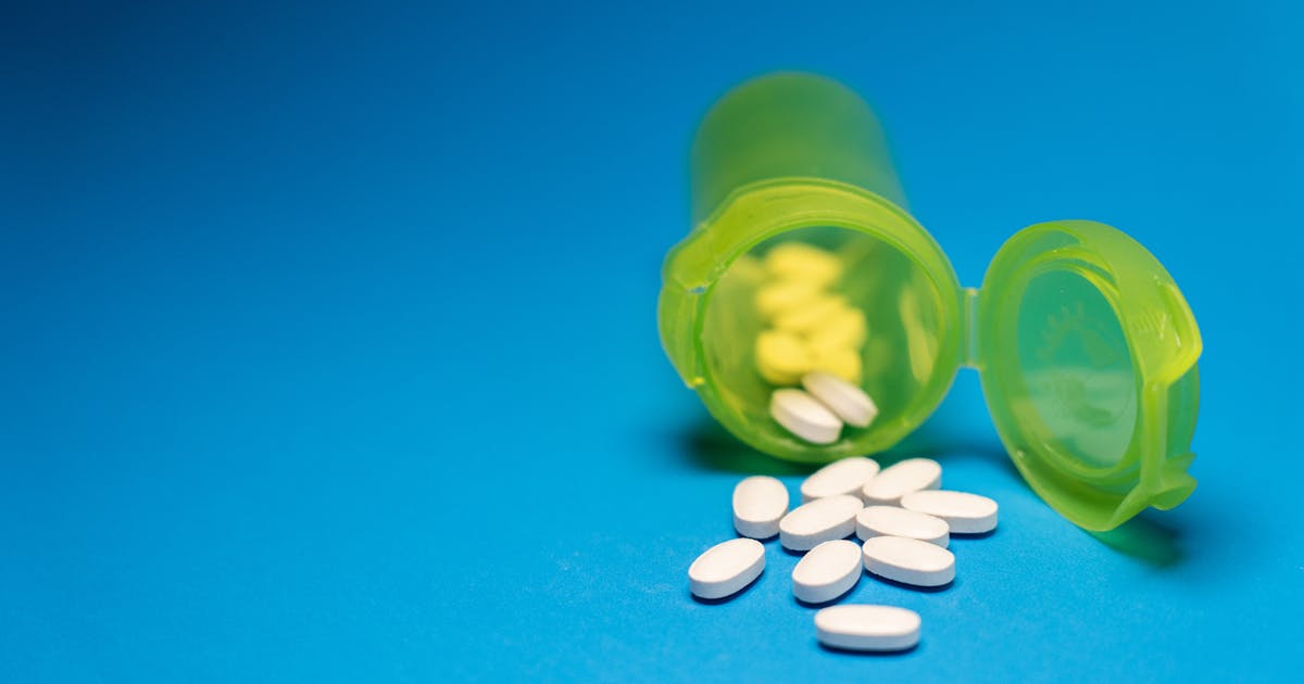 Green pill bottle with white tablets scattered on a blue background symbolizing medication