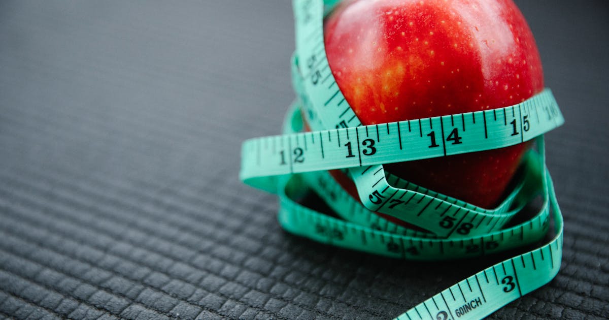 A vibrant red apple encircled by a blue measuring tape symbolizing health and weight management