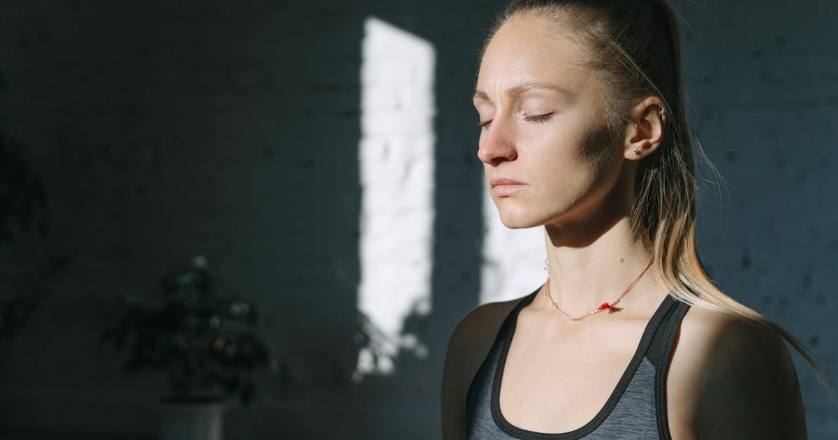 A woman in meditation inside a sunlit room, eyes closed, feeling calm and peaceful