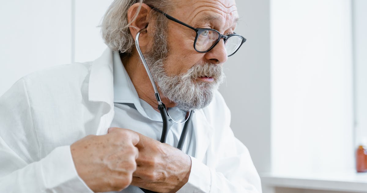 Senior male doctor checking health with stethoscope indoors