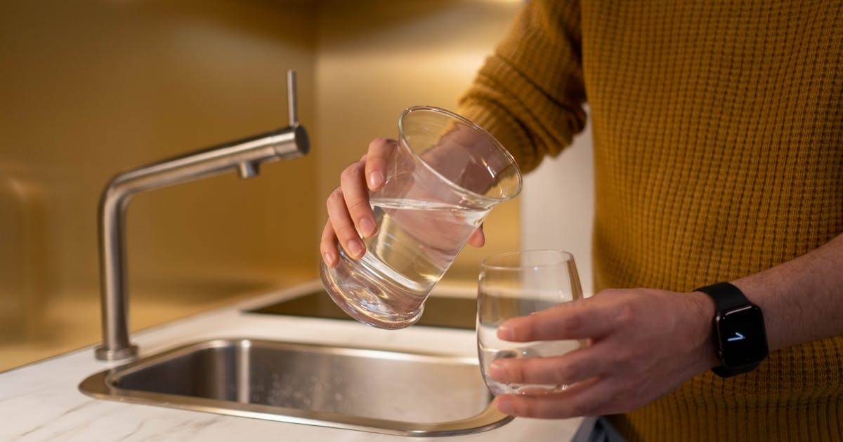 Person pouring water from a pitcher into a glass in a contemporary kitchen setting