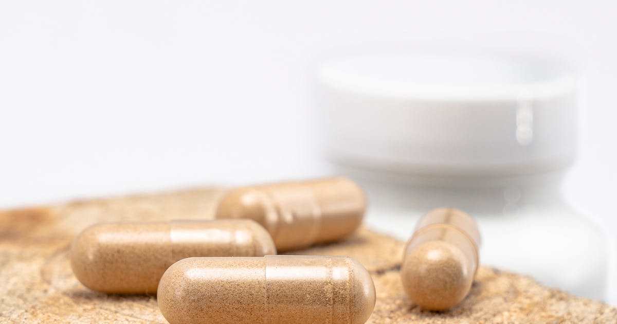 Brown supplement capsules placed on a wooden surface with a blurred bottle in the background