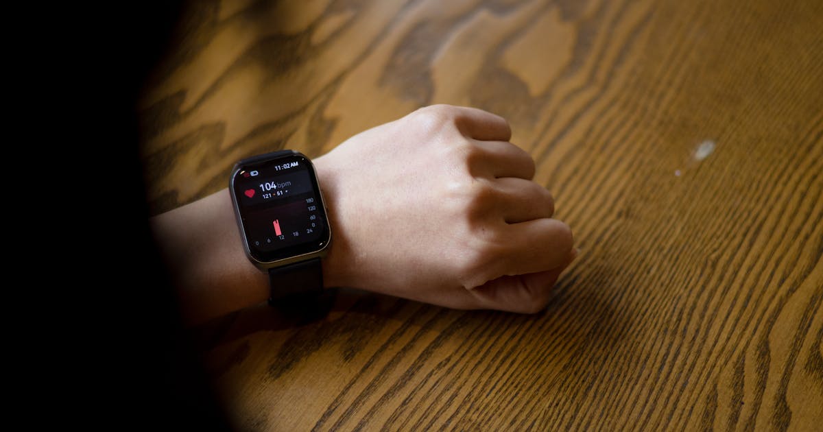 A person checks heart rate on a smartwatch showing the reading on a wooden table