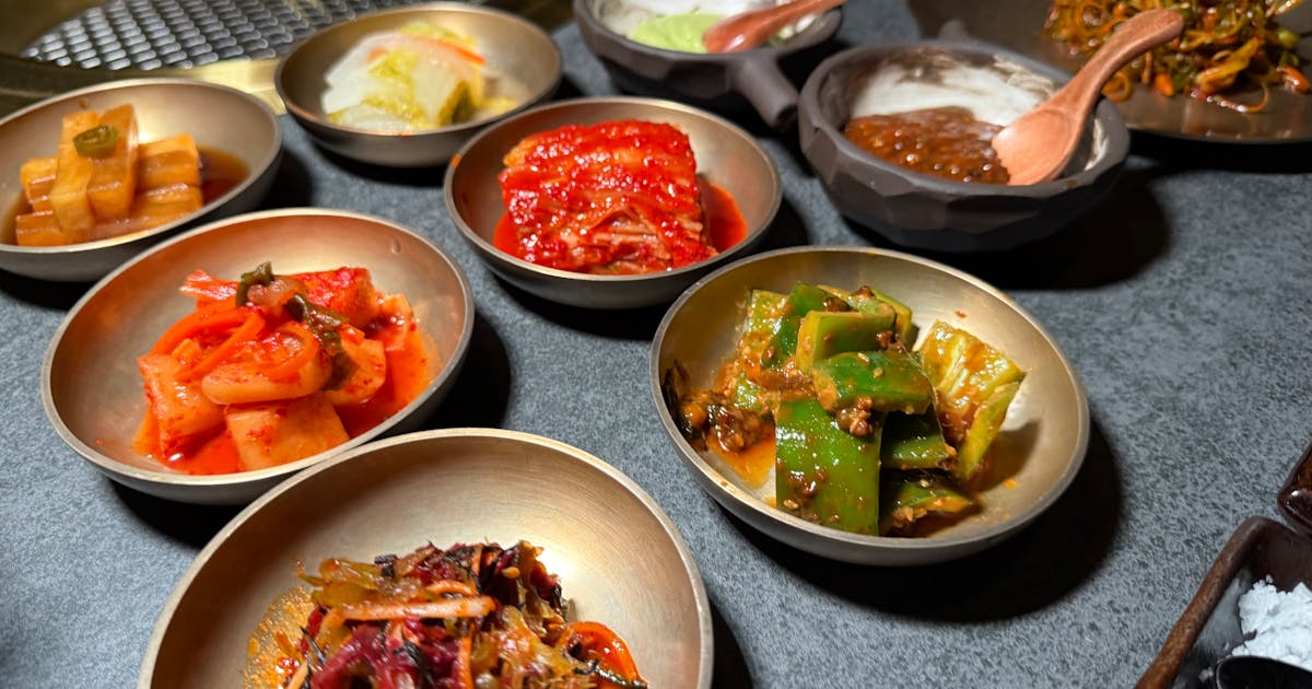 Variety of Korean banchan side dishes including kimchi served in metallic bowls on a table