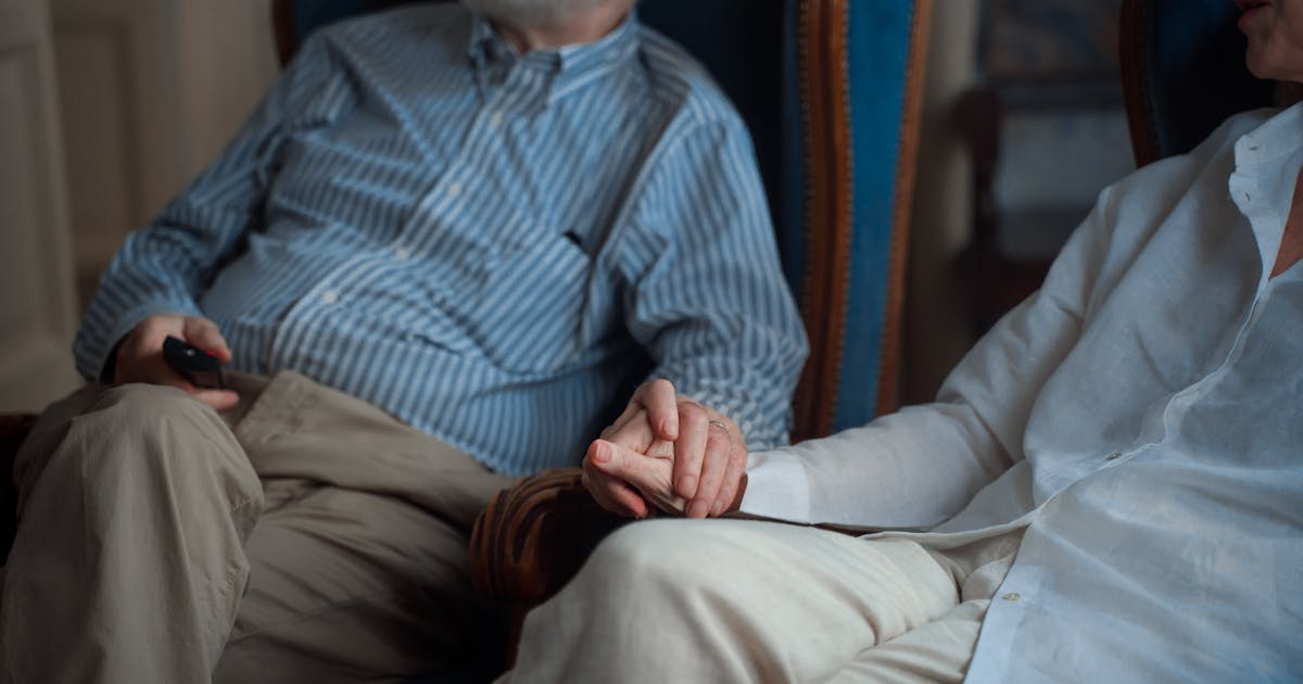An elderly couple sitting together, holding hands in a cozy room, symbolizing companionship