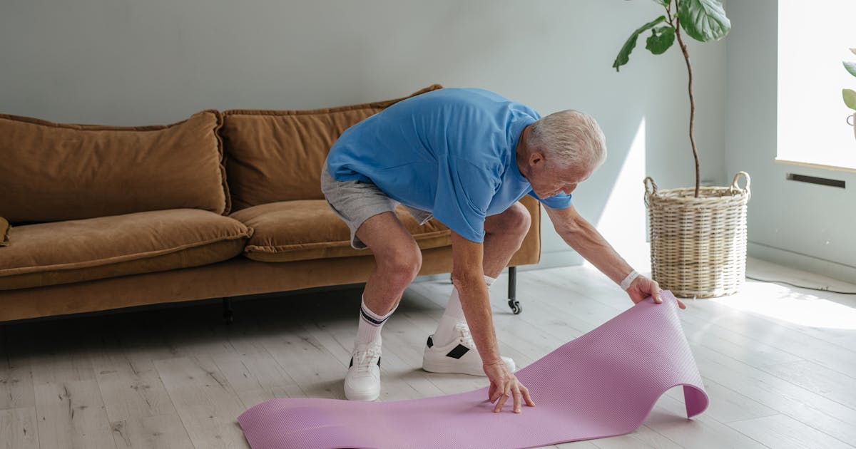 An elderly man sets up his yoga mat indoors, embodying a healthy lifestyle