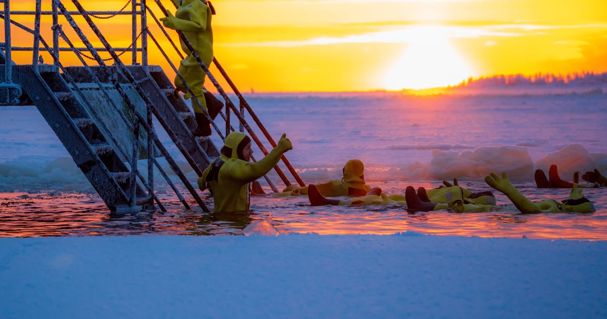 Group of people in colorful suits ice bathing at sunrise with vibrant sky above