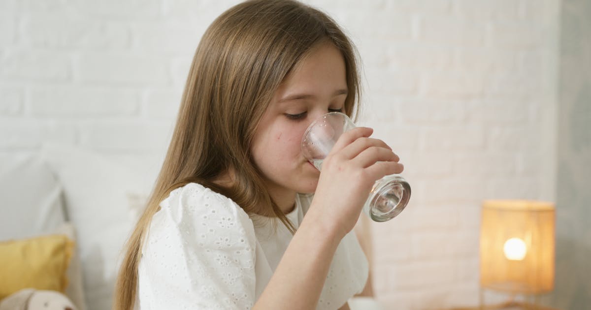 Woman drinking a glass of water in natural light for heart-healthy hydration