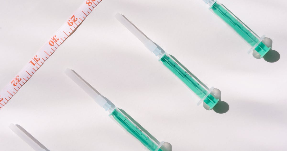 Top view of green filled syringes and measuring tape on a white background, emphasizing healthcare themes