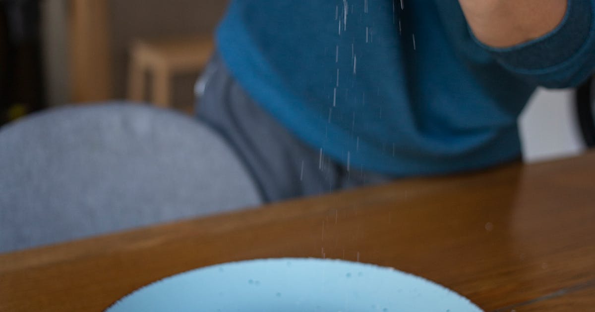 Hand sprinkling salt on a sunny side up egg on a blue plate, breakfast scene