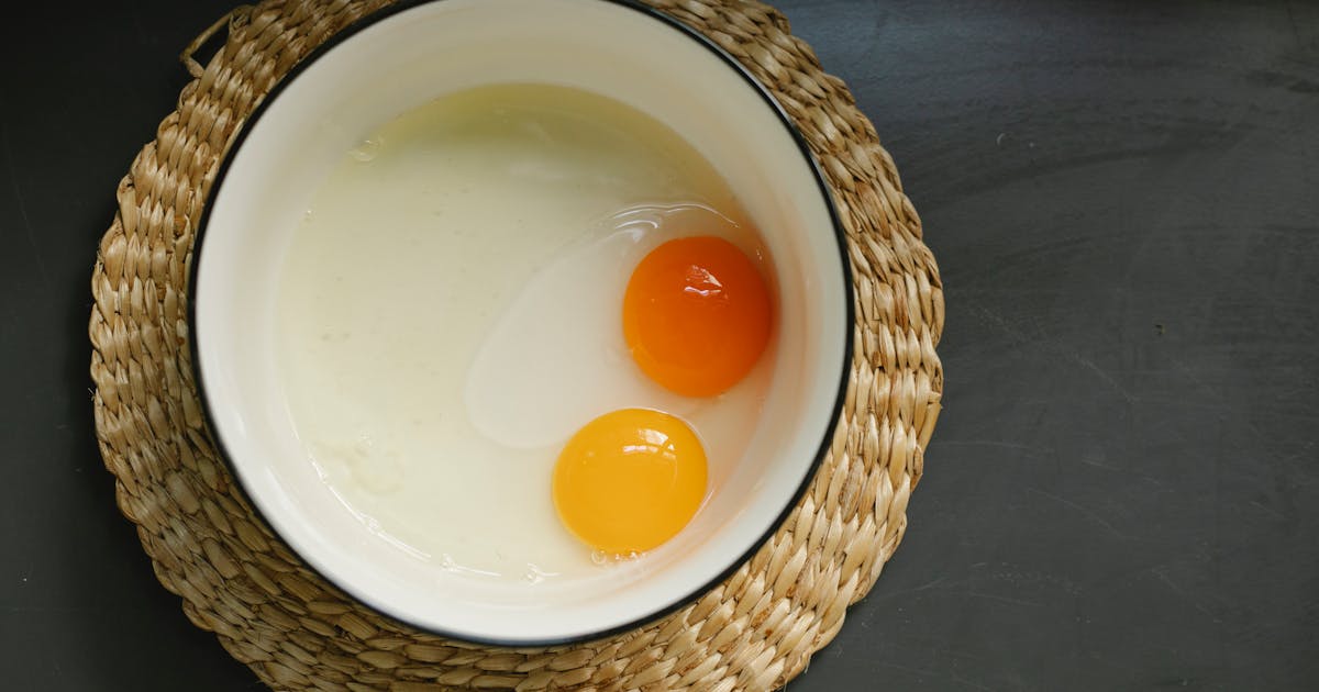 Close-up of a single cracked egg with yolk separated, on a light surface