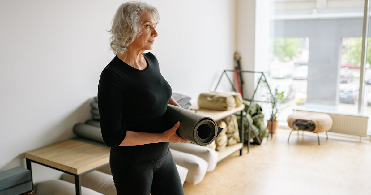 Mature woman holding a yoga mat in a bright studio