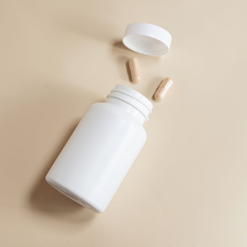 An open supplement bottle with two capsules on a neutral surface