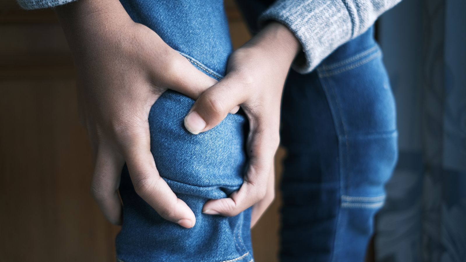 A person holding their knee with both hands, indicating joint pain