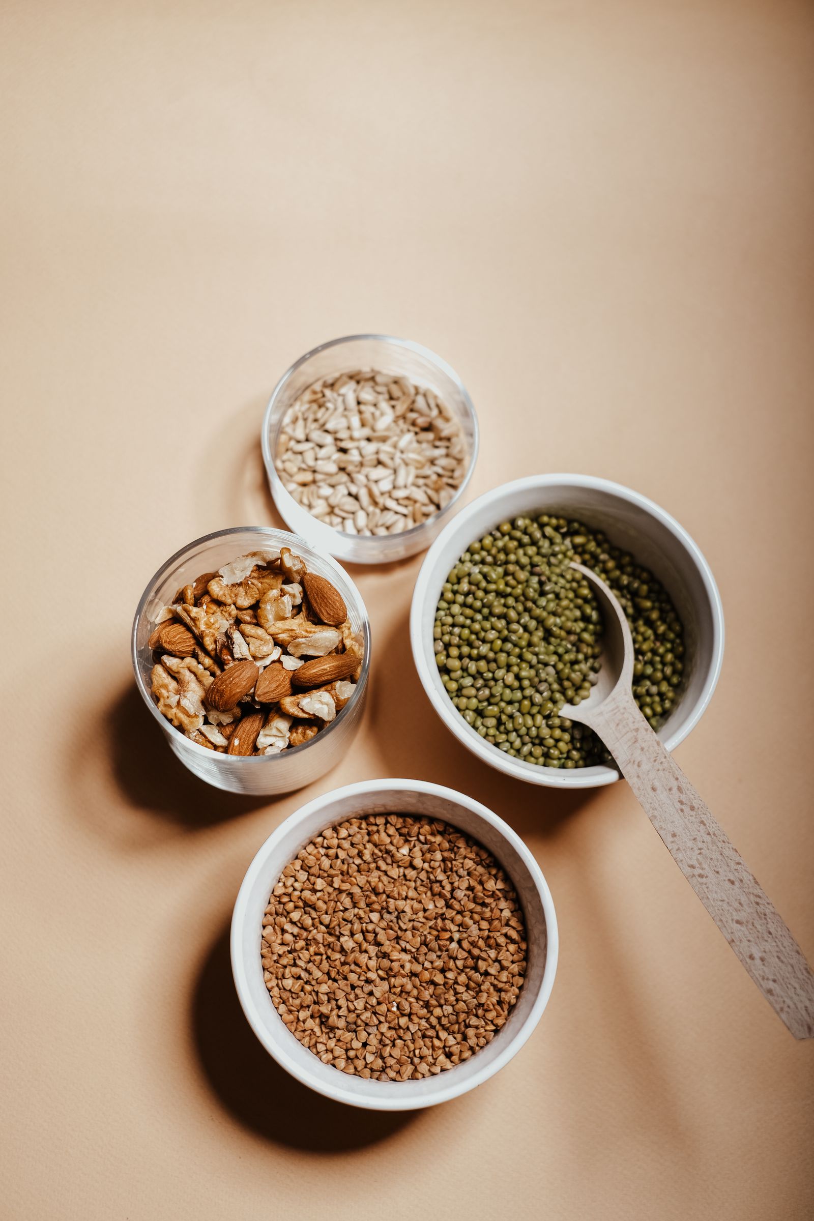 Bowls of mung beans, buckwheat, nuts and seeds on a plain background